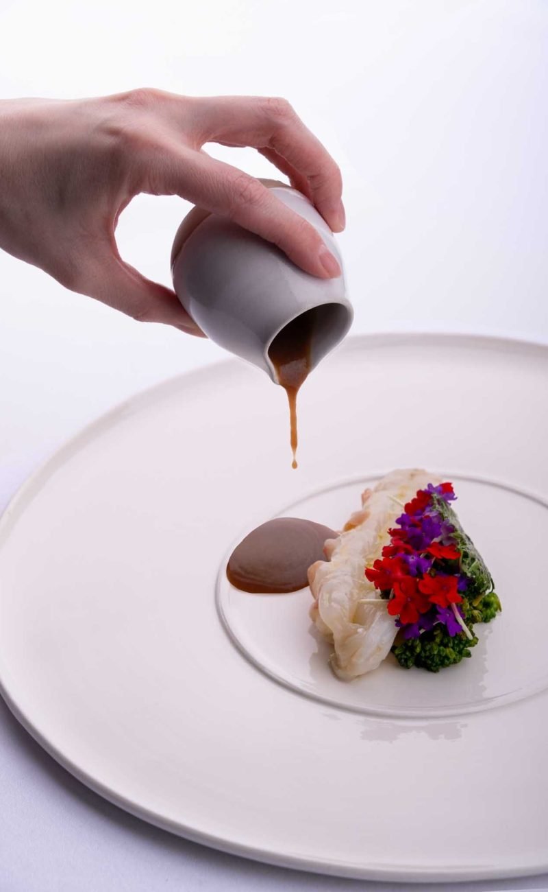 Un geste délicat de verser une sauce onctueuse sur un plat cinq étoiles photographe à NANTES
